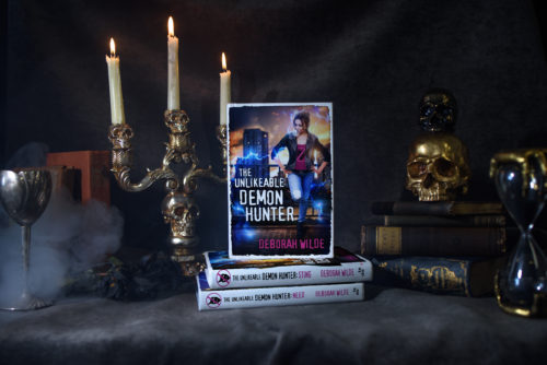 3 copies of The Unlikeable Demon Hunter stacked on a table with a candelabra.